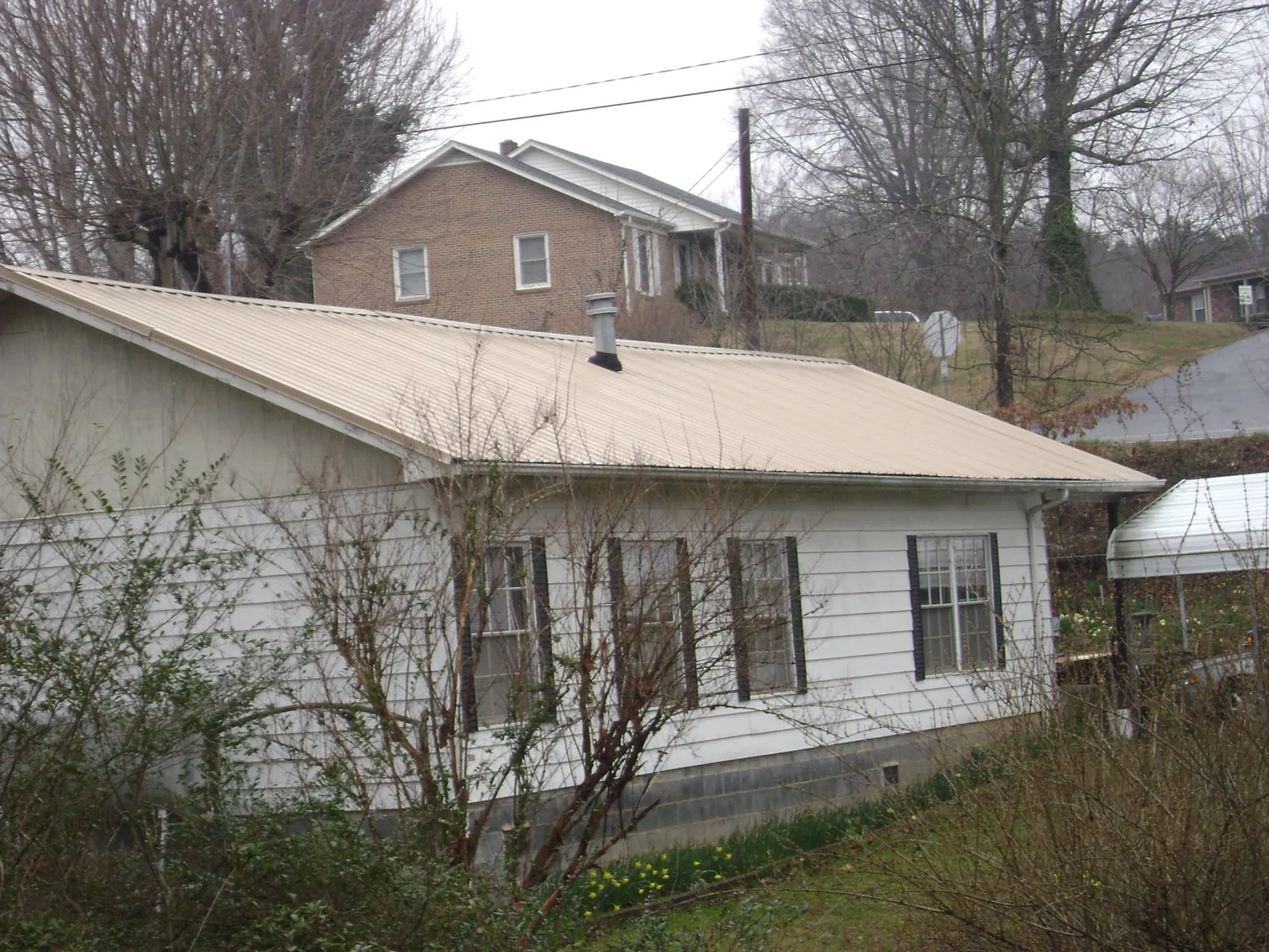 Tan metal roof on a white sided house set into a hillside — Commercial Roofing by Roofing Brothers in Goshen