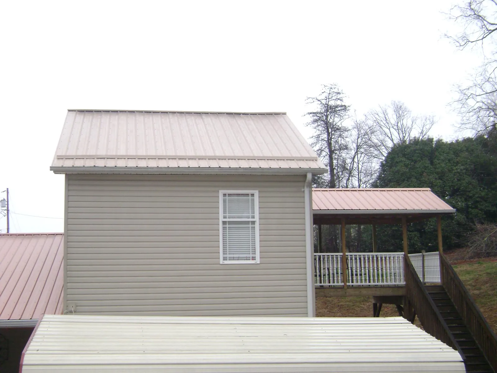 Tan metal roofs on a two story addition and attached porch, from a Roof Replacement job in Goshen