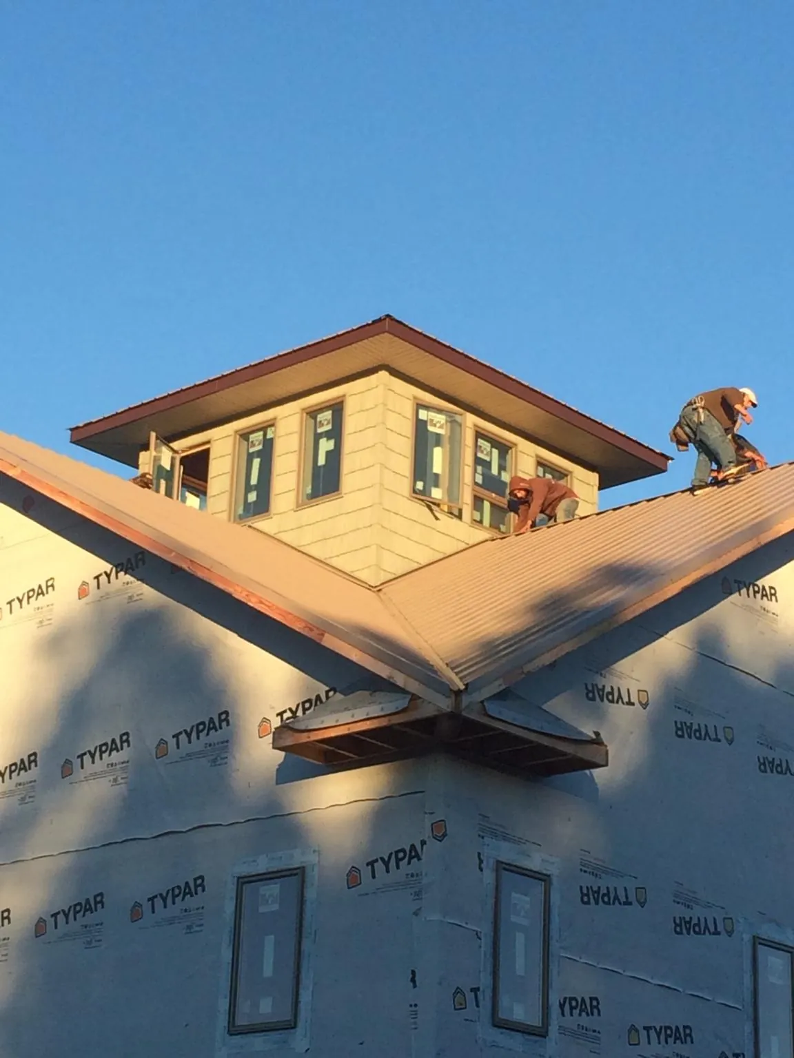 Roofers working around a rooftop cupola on a new metal roof at sunset — Roof Waterproofing in Goshen by Roofing Brothers